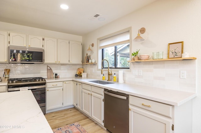 kitchen with white cabinets, appliances with stainless steel finishes, light hardwood / wood-style floors, sink, and backsplash