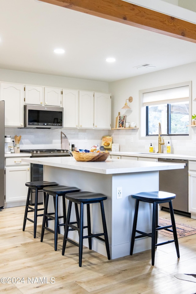 kitchen with white cabinets, a kitchen island, stainless steel appliances, light hardwood / wood-style floors, and a breakfast bar area