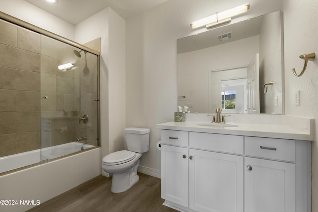 full bathroom with hardwood / wood-style flooring, combined bath / shower with glass door, vanity, and toilet