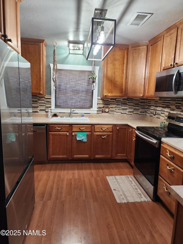 kitchen featuring visible vents, brown cabinets, stainless steel appliances, light wood-type flooring, and a sink