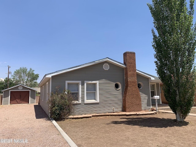 ranch-style home featuring a chimney, dirt driveway, a storage unit, a garage, and an outdoor structure