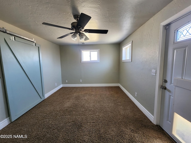 unfurnished bedroom featuring a textured ceiling, dark colored carpet, a textured wall, and baseboards