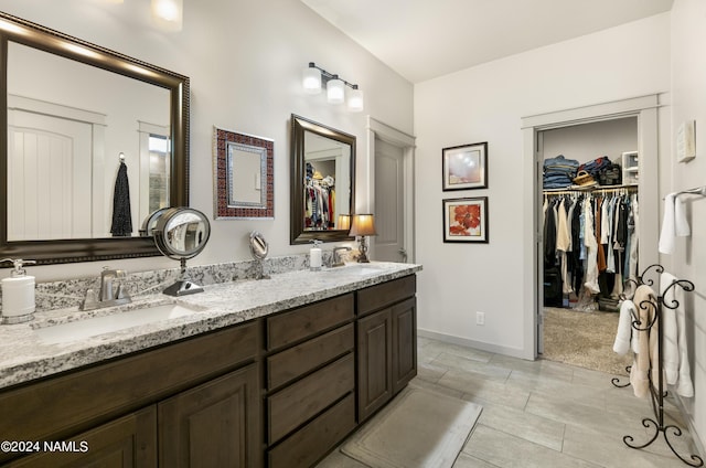 bathroom with double vanity, a sink, a spacious closet, and baseboards
