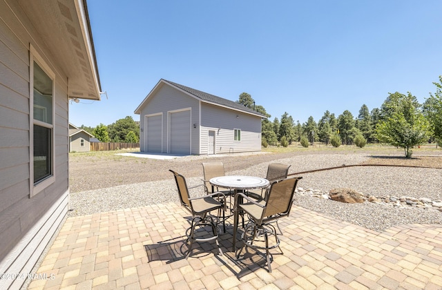 view of patio featuring a detached garage, outdoor dining area, and an outbuilding
