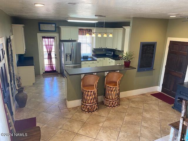 kitchen featuring a breakfast bar area, white cabinetry, stainless steel fridge with ice dispenser, kitchen peninsula, and pendant lighting