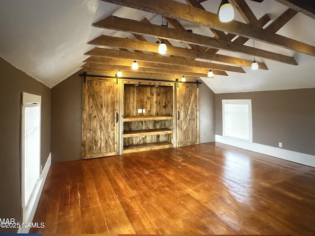 additional living space with a barn door, hardwood / wood-style floors, and vaulted ceiling with beams