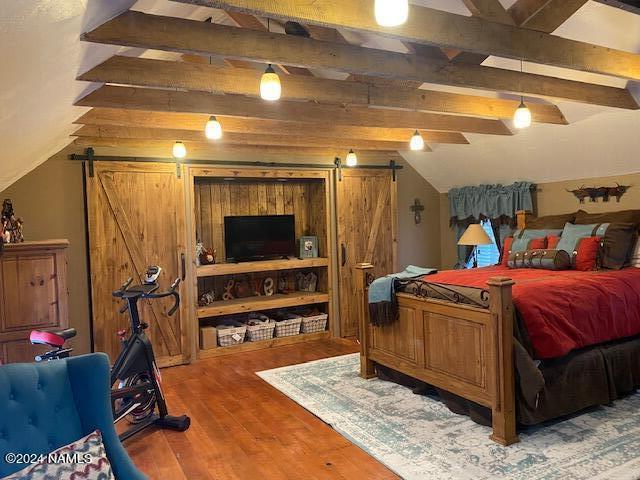 bedroom featuring hardwood / wood-style flooring, a barn door, and lofted ceiling with beams