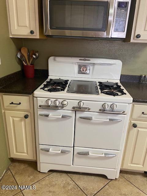 kitchen with double oven range, cream cabinets, and light tile patterned floors