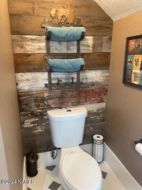 bathroom with lofted ceiling, toilet, a textured ceiling, and wood walls