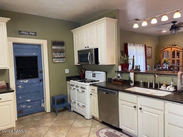 kitchen with appliances with stainless steel finishes, sink, white cabinets, light tile patterned floors, and ceiling fan