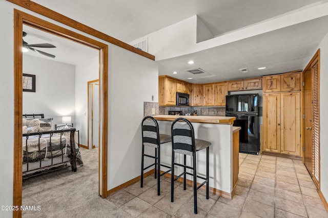 kitchen featuring a kitchen bar, light carpet, kitchen peninsula, decorative backsplash, and black appliances