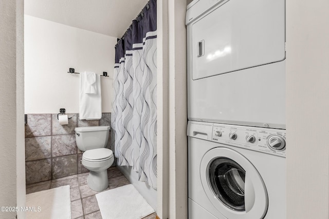 laundry room with tile walls, light tile patterned floors, and stacked washer / dryer