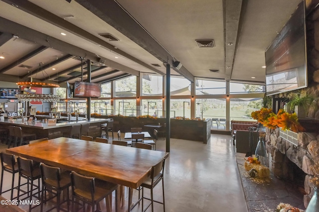 dining space featuring concrete flooring, lofted ceiling with beams, and bar