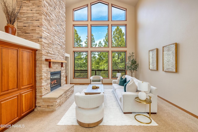 living area featuring light carpet, a stone fireplace, a high ceiling, and baseboards