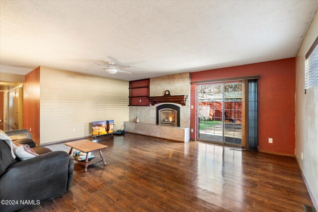 living room with a large fireplace, ceiling fan, a textured ceiling, and dark hardwood / wood-style flooring