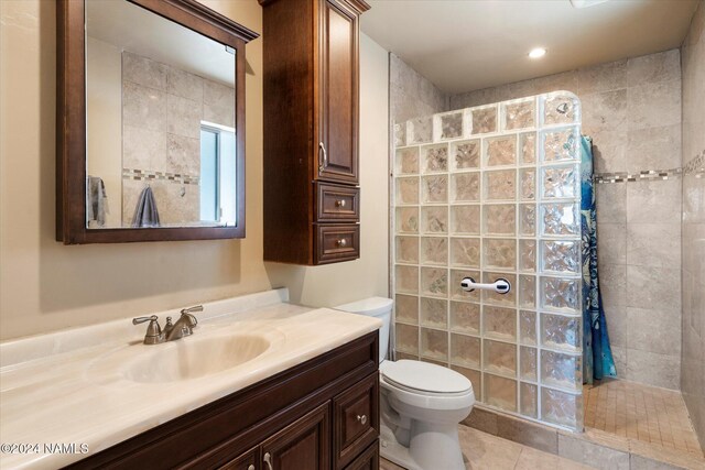 bathroom with a tile shower, toilet, tile patterned floors, and vanity