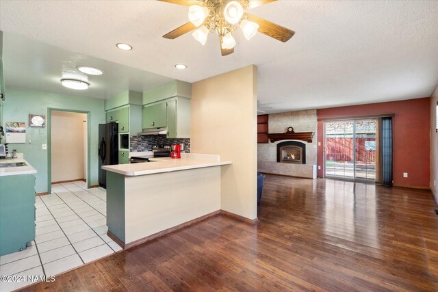 kitchen with decorative backsplash, electric stove, a large fireplace, kitchen peninsula, and black fridge with ice dispenser