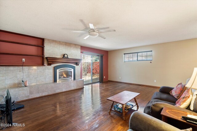 living room with ceiling fan, hardwood / wood-style floors, a textured ceiling, and a tiled fireplace