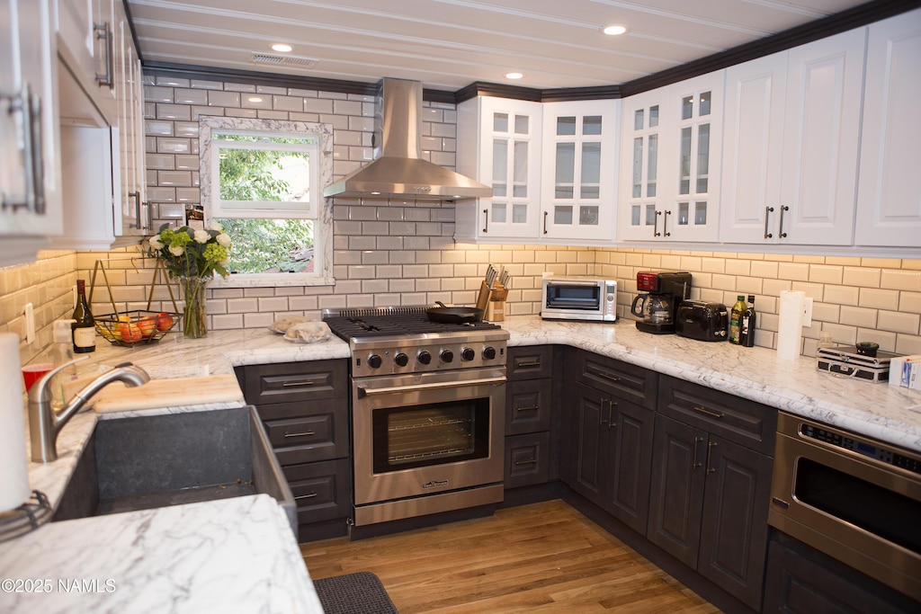 202 S Wc Riles St, Flagstaff, AZ 86001 - kitchen featuring wall chimney exhaust hood, appliances with stainless steel finishes, white cabinetry, light stone countertops, and backsplash