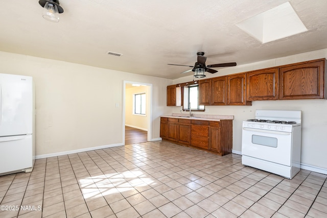 kitchen featuring a textured ceiling, white appliances, a skylight, light tile patterned flooring, and ceiling fan