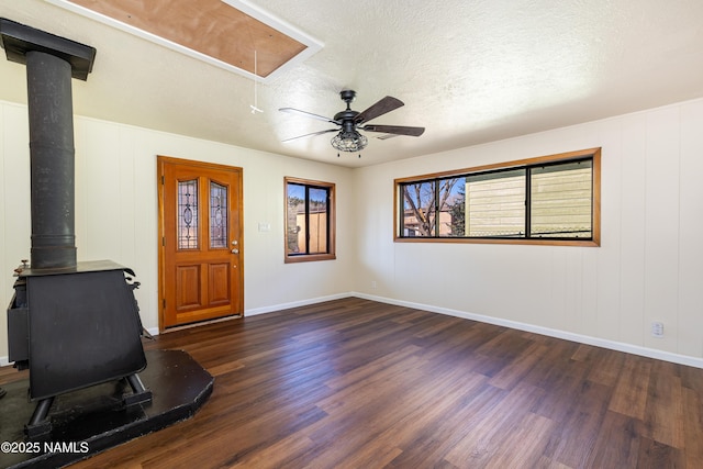 interior space with a wood stove, ceiling fan, a textured ceiling, and dark hardwood / wood-style flooring