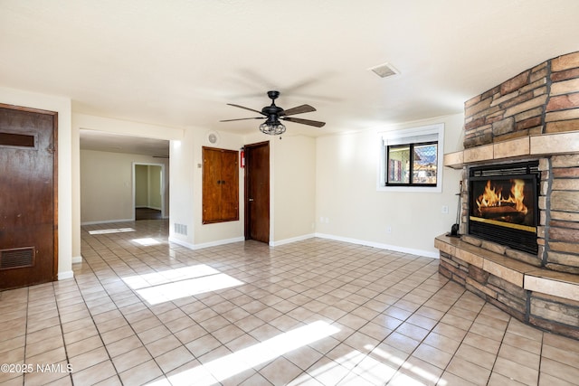 unfurnished living room with ceiling fan, a stone fireplace, and light tile patterned floors