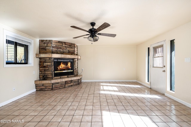 unfurnished living room featuring ceiling fan, light tile patterned flooring, a wealth of natural light, and a fireplace