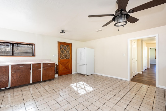 interior space with dark brown cabinets, light tile patterned floors, ceiling fan, and white fridge