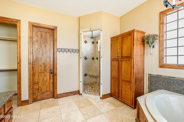 bathroom with tile patterned flooring, a bath, baseboards, and tiled shower