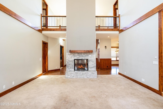 unfurnished living room with a stone fireplace, a high ceiling, baseboards, and carpet floors