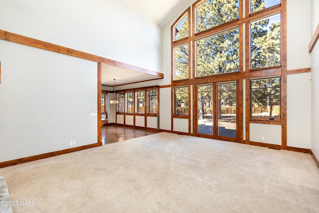 unfurnished living room featuring carpet flooring, high vaulted ceiling, and baseboards