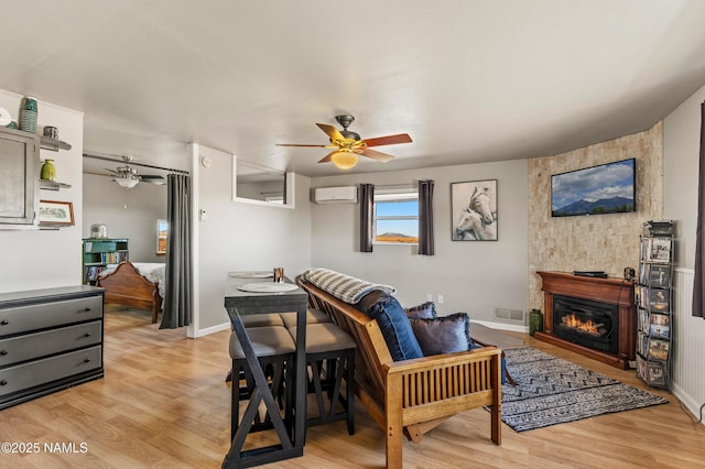 interior space with ceiling fan, light wood finished floors, a wall mounted AC, and visible vents