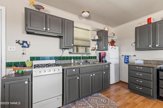 kitchen featuring light wood-style floors, dark countertops, white appliances, and a sink