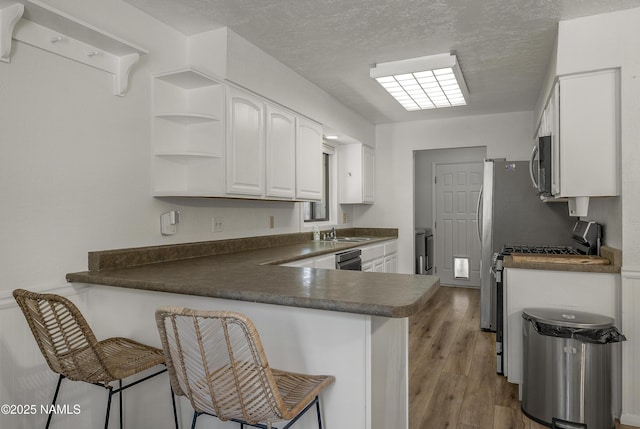 6320 N Mountaineer Rd, Flagstaff, AZ 86004 - kitchen with stainless steel appliances, a peninsula, dark countertops, white cabinets, and a textured ceiling