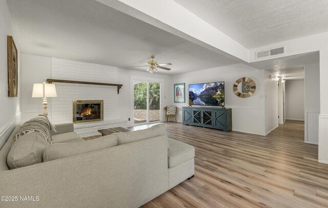 6320 N Mountaineer Rd, Flagstaff, AZ 86004 - living room with wood finished floors, a textured ceiling, a brick fireplace, a ceiling fan, and a wainscoted wall