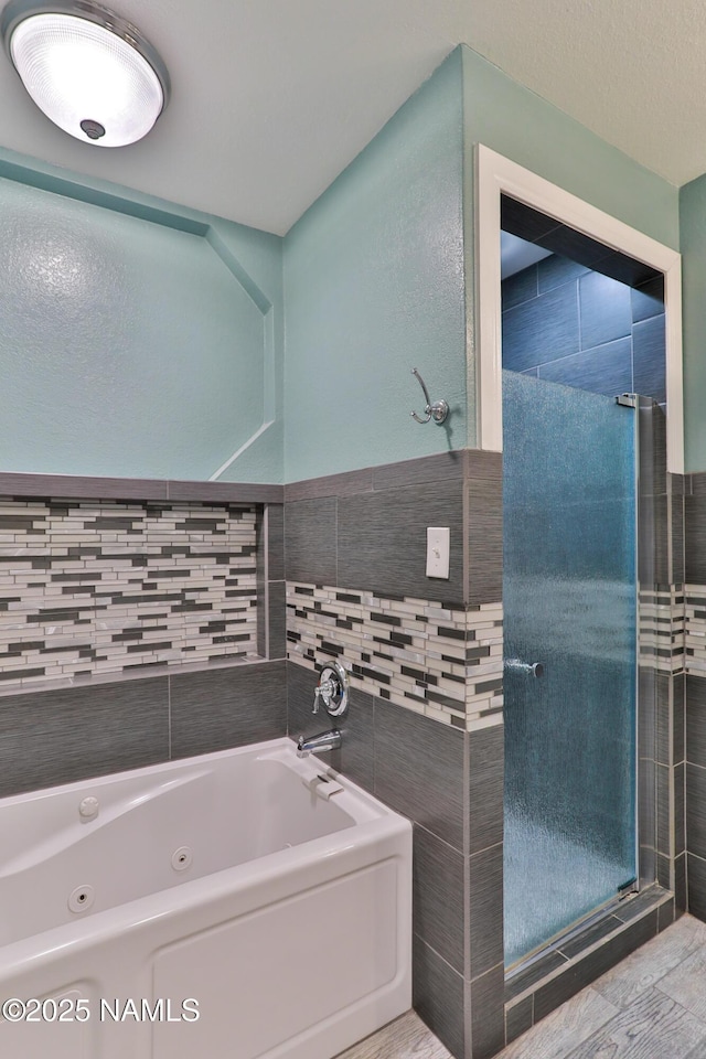 bathroom featuring a stall shower, a tub with jets, and tile walls