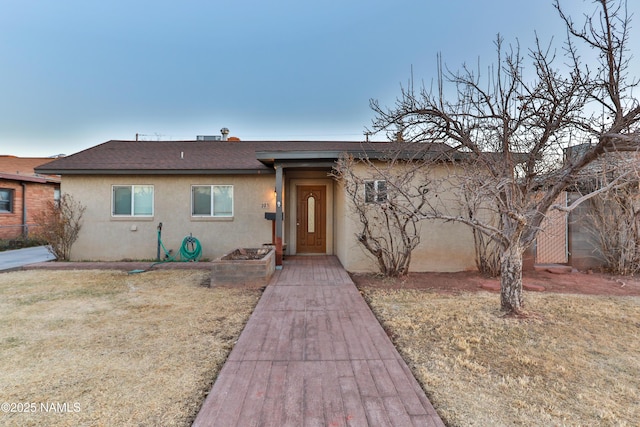 single story home featuring a front yard, roof with shingles, and stucco siding