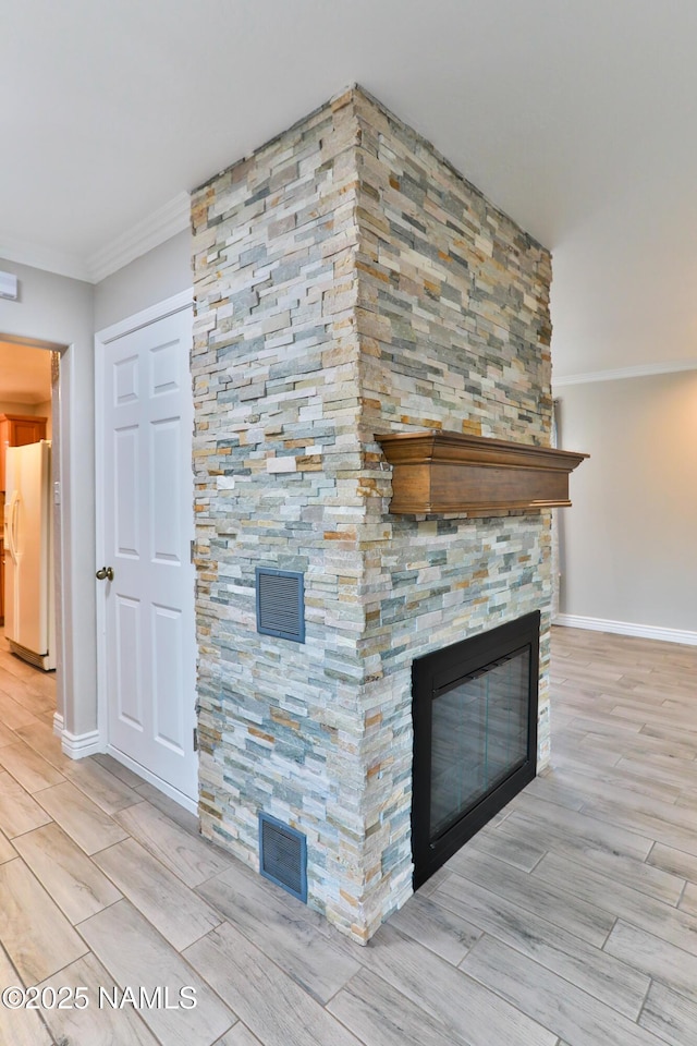 unfurnished living room featuring ornamental molding, wood finish floors, visible vents, and a stone fireplace