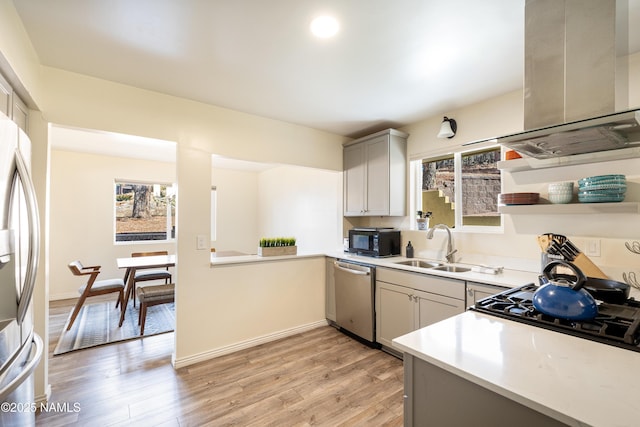 kitchen featuring island range hood, a sink, light countertops, appliances with stainless steel finishes, and light wood finished floors