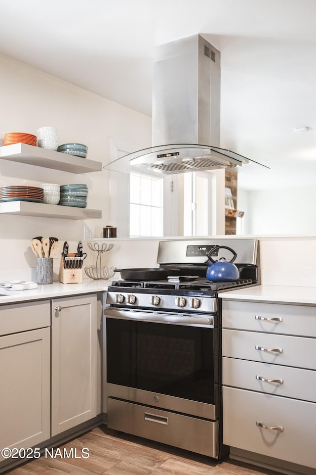 kitchen featuring stainless steel gas range, island exhaust hood, light countertops, and light wood-style floors