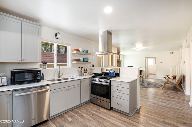 kitchen featuring a peninsula, island exhaust hood, gray cabinets, stainless steel appliances, and a sink