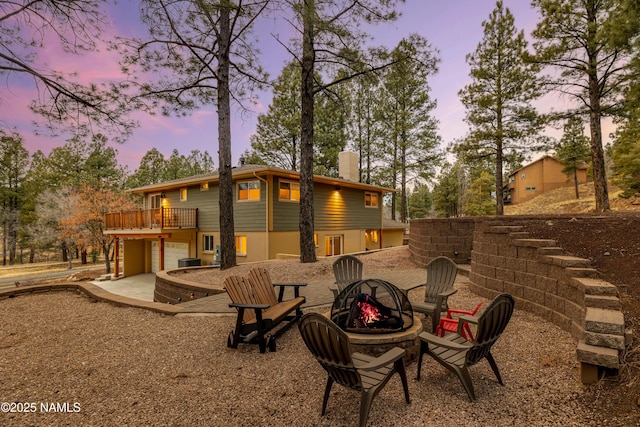 back of house at dusk with an outdoor fire pit, a wooden deck, stucco siding, a chimney, and a patio area