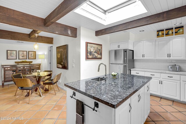 kitchen featuring white cabinets, stainless steel refrigerator, beam ceiling, and a center island with sink