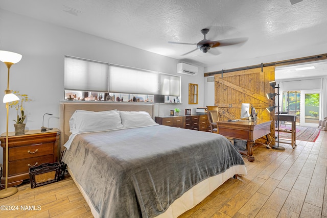 bedroom with ceiling fan, a textured ceiling, a wall mounted AC, and a barn door