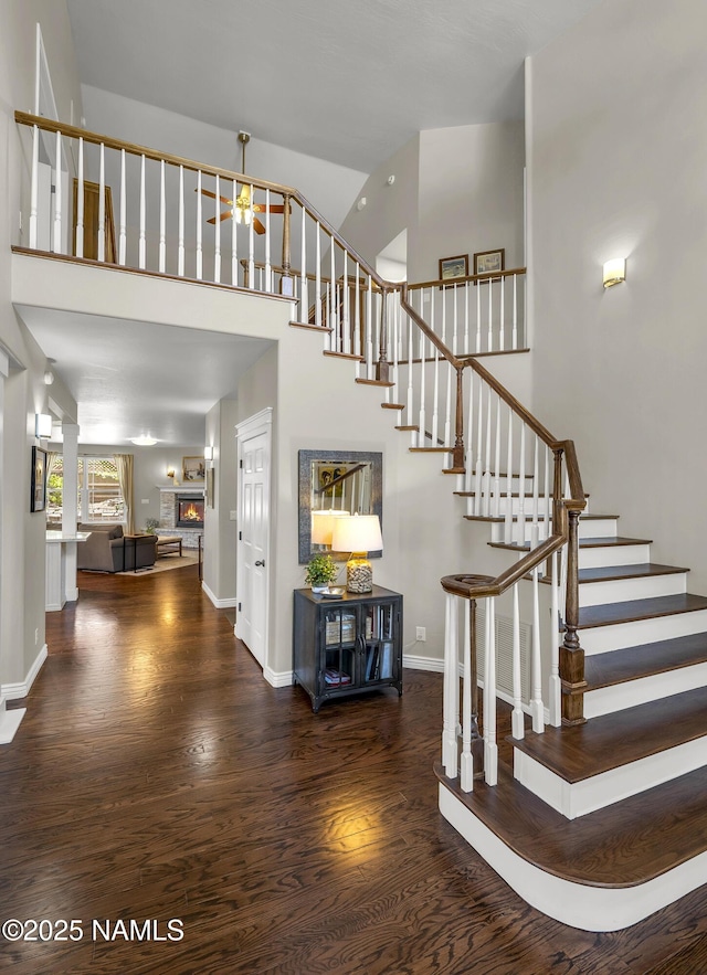1085 N Conifer Rd, Flagstaff, AZ 86001 - stairway with wood finished floors, a ceiling fan, baseboards, a high ceiling, and a warm lit fireplace