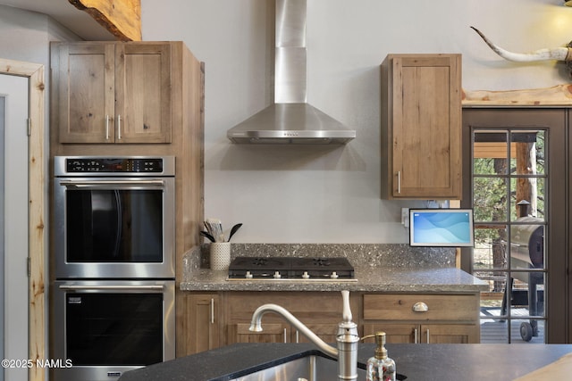 kitchen featuring a sink, wall chimney exhaust hood, dark stone countertops, and stainless steel appliances