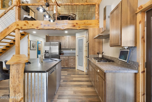 kitchen with a kitchen island with sink, dark countertops, appliances with stainless steel finishes, a sink, and dark wood-type flooring