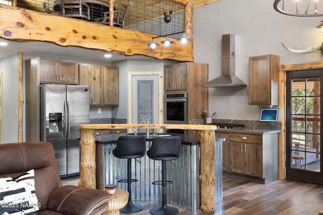 kitchen featuring dark wood-style flooring, a kitchen island, a kitchen bar, wall chimney exhaust hood, and stainless steel appliances
