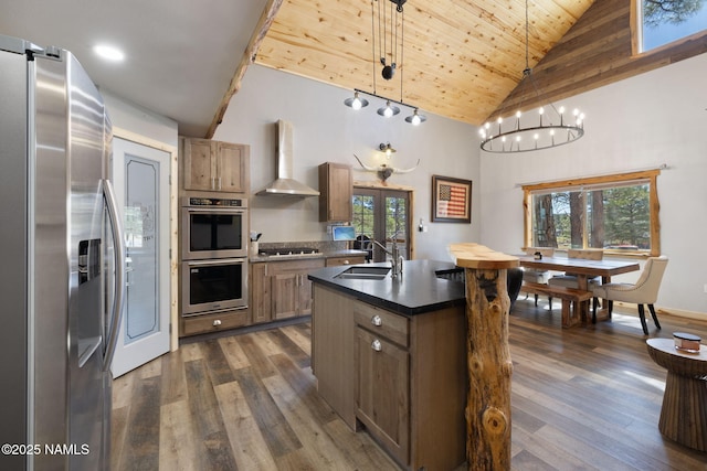 kitchen with wall chimney range hood, dark wood-style flooring, dark countertops, high vaulted ceiling, and stainless steel appliances