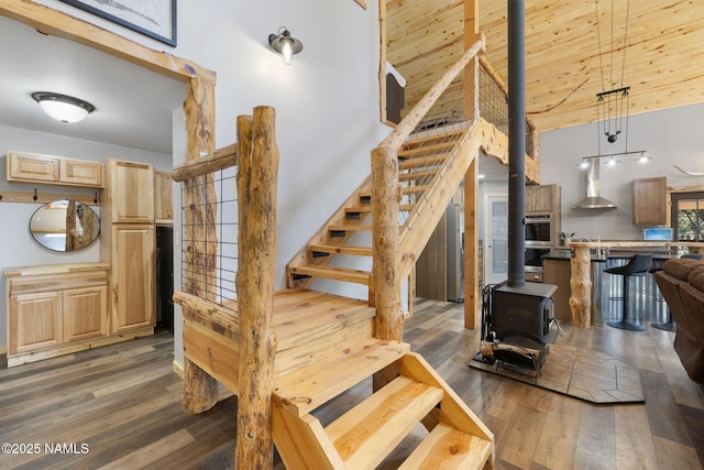 stairs with a wood stove, wood finished floors, and a towering ceiling